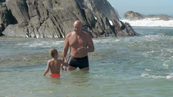 Папа с маленьким ребенком весело провести время в чистом океане воды на скалах — стоковое видео