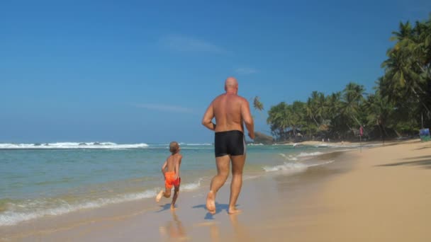 Familia con papá e hijo corre a lo largo de la playa de mar cámara lenta — Vídeos de Stock