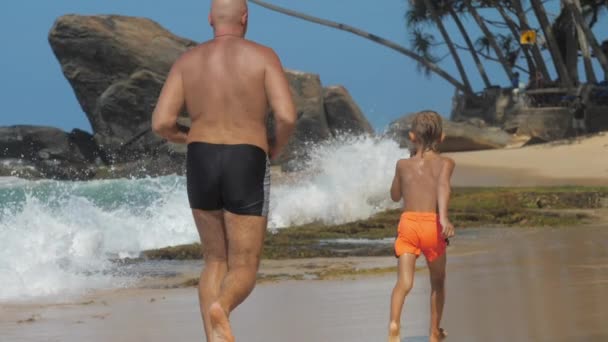 Мальчик проводит время с папой бегая по красивому пляжу — стоковое видео