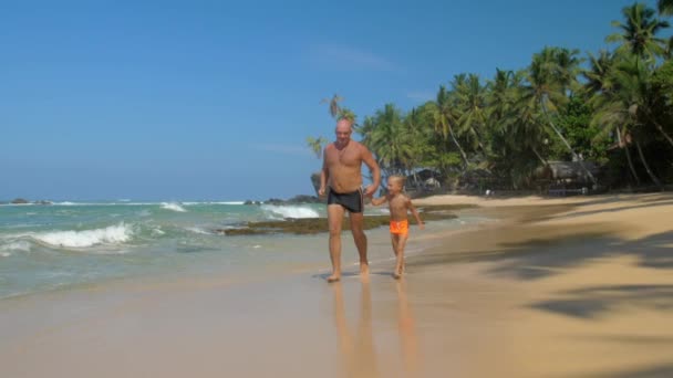 Vater und Sohn rennen Hand in Hand am schönen Meeresstrand entlang — Stockvideo
