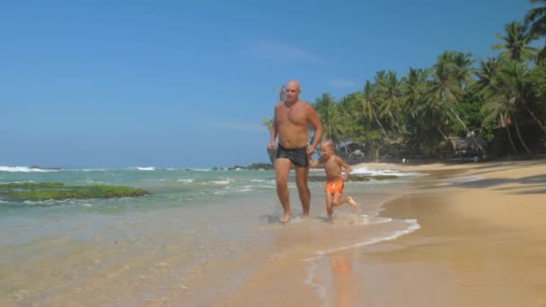 父と息子の家族は、エキゾチックな海の海岸に沿って実行されます — ストック動画
