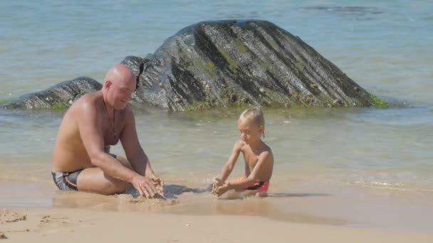 Kleiner Sohn und Papa haben Spaß mit nassem Sand an der Surfleine — Stockvideo