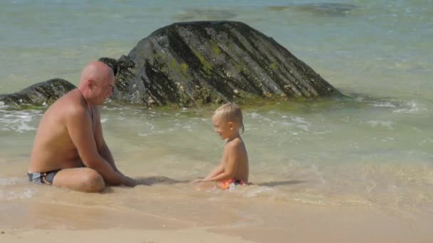 아버지와 아들의 가족은 해변에서 맑은 바닷물에 달려 있습니다. — 비디오
