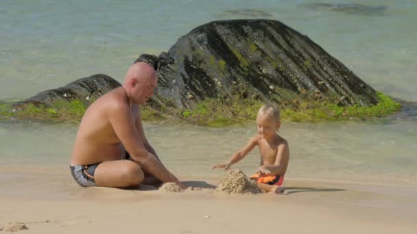Vater spielt mit Sohn, der in Ozean-Zeitlupe nassen Sand schaufelt — Stockvideo