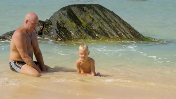 Far stänk vatten på son leker med våt sand i havet — Stockvideo