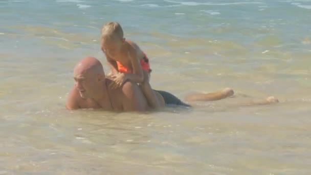 Батько штовхає маленького сина назад у океанічну воду — стокове відео