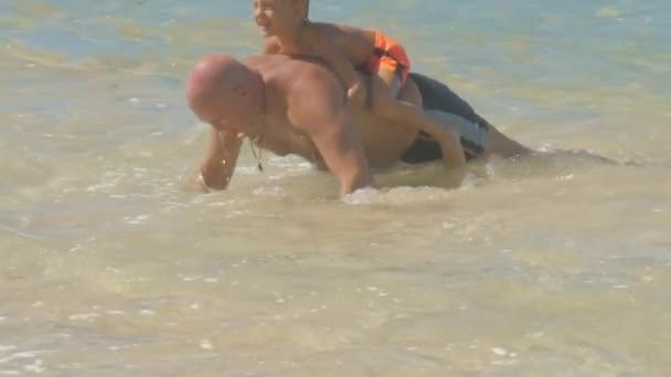 Pai faz exercício esportivo com filho nas costas em mar azul — Vídeo de Stock