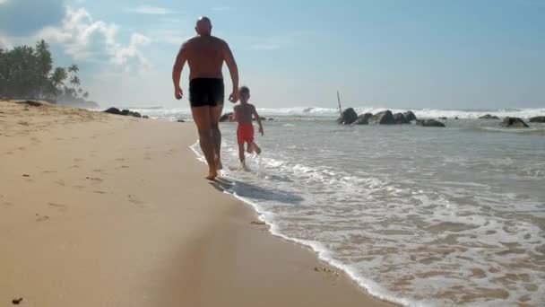 Tata i chłopiec biegać wzdłuż mokrej plaży w ośrodku powolny — Wideo stockowe