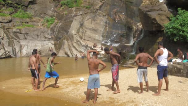 Mann kickt weißen Ball an Freund im Wasser gegen Klippe — Stockvideo