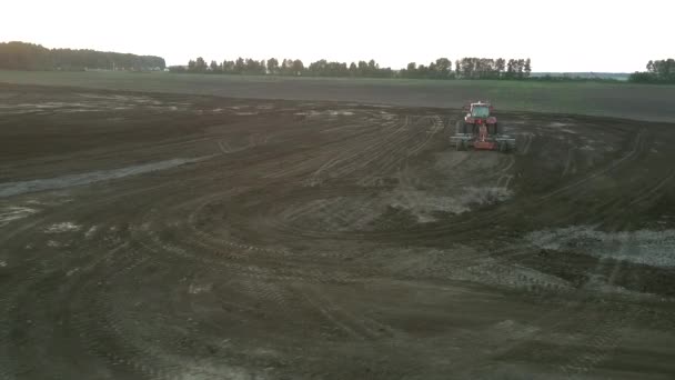 Red tractor plows field soil at sunset bird eye view — Stock Video