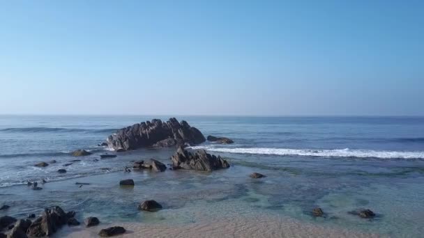 Błękitne wody oceanu otaczają brązowe skały na piaszczystym wybrzeżu — Wideo stockowe