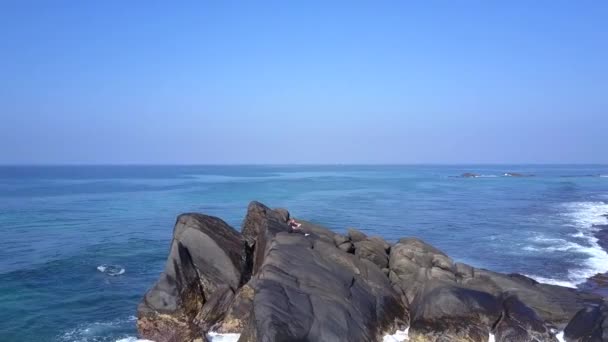 Girl sits in yoga pose on large rocky cliff washed by ocean — Stock Video