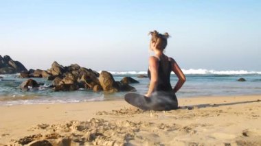 Siyah eşofmanlı sporcu kız mavi okyanusa uzanıyor.