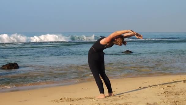 Sportieve dame oefeningen op zandstrand op golvende oceaan — Stockvideo