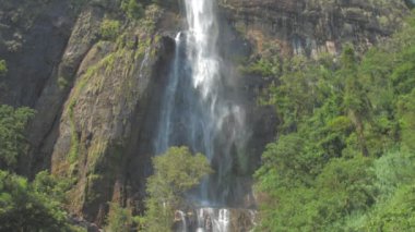 Su, kahverengi ve yeşil renkli büyük kayalık kayalıklardan düşer.