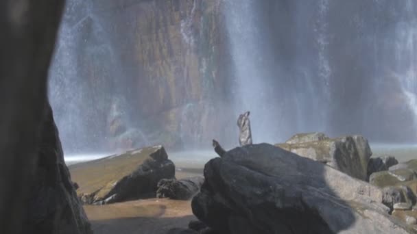 Waterval door natte stenen verschijnt van achter bruine rots — Stockvideo
