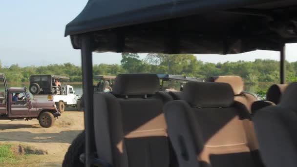Vehículos conducen a lo largo de camino de tierra marrón contra lago — Vídeo de stock