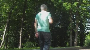 Adam ara sokakta yürüyor, bahar parkında yeşil bitkilerin tadını çıkarıyor.