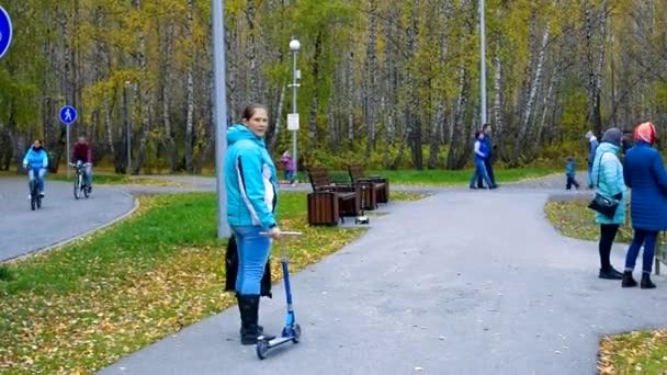 어머니가 어린 스쿠터 아이를 데리고 공원 트랙을 달리고 있는 모습 — 비디오