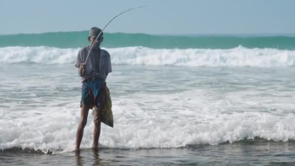 Місцевий чоловік тримає рибальський стрижень в руці проти махаючого океану — стокове відео