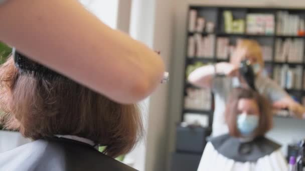 Досвідчений перукар у масці сушить короткі темні пасма волосся — стокове відео