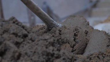 İnsan ıslak çimentoyla yerdeki metal küreği karıştırır.