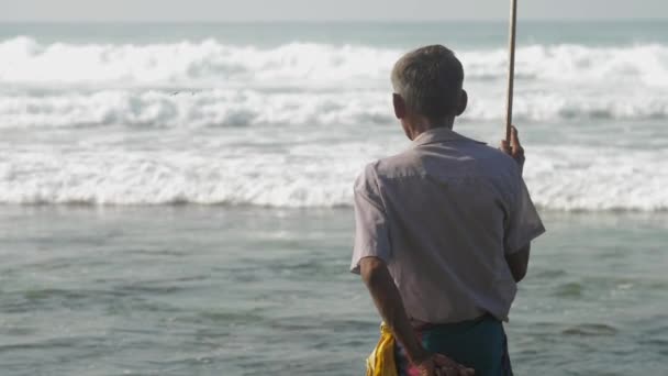 Рибалка тримає рибальський стрижень в руці і йде проти океану — стокове відео