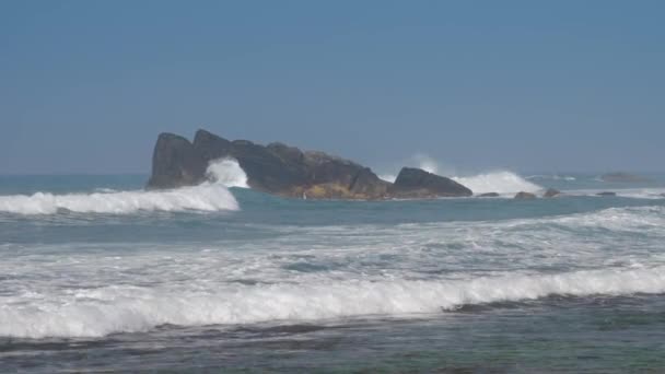Ondeggiando oceano blu con alghe verdi contro grandi rocce — Video Stock