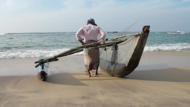 Homem puxa barco de pesca artesanal tradicional contra o mar — Vídeo de Stock