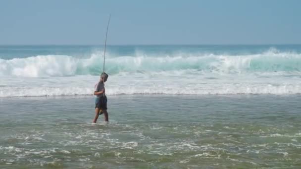 Lokale visser houdt hengel in de hand in zwaaiende blauwe oceaan — Stockvideo