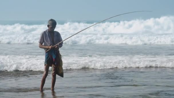 Hombre local tiene caña de pescar en la mano contra el océano ondulante — Vídeos de Stock