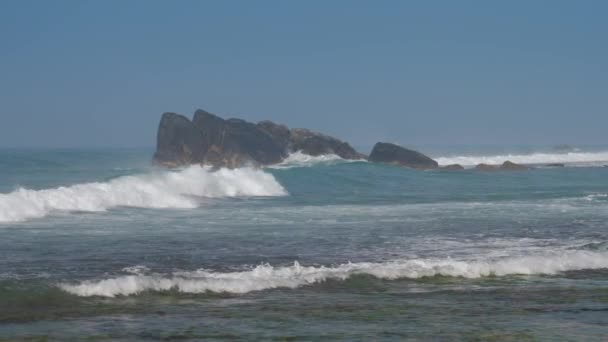 Ondeggiando oceano blu con alghe verdi contro grandi rocce — Video Stock