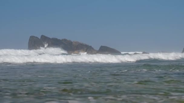 Ondeggiando oceano blu con alghe verdi contro grandi rocce — Video Stock