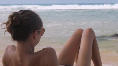 Sıska kadın güneş gözlüğü takıyor ve dalgalı okyanusu gözlemliyor.