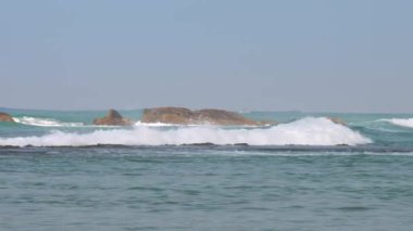 Açık mavi gökyüzüne karşı ağır dalgalar ve taşlarla okyanus