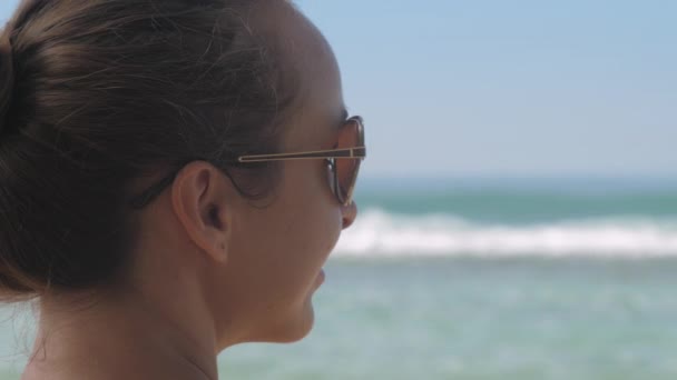 Slanke dame draagt een zonnebril en observeert golvende oceaan — Stockvideo
