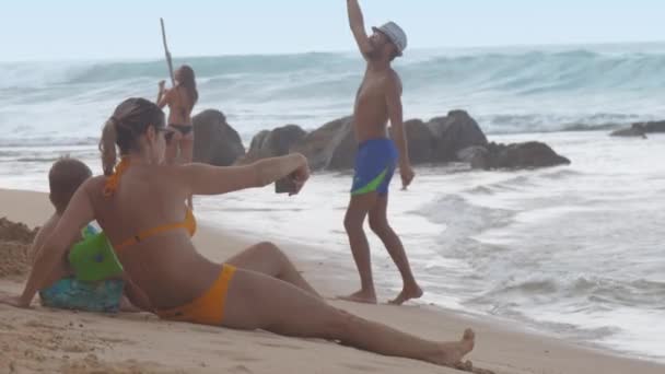 Señora se sienta en la playa arena cerca de niño en brazo flota contra el océano — Vídeo de stock