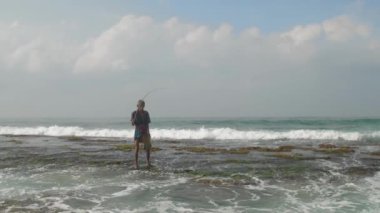 Yaşlanmış Sinhalese 'li adam, okyanusta yavaşça ahşap olta atıyor.