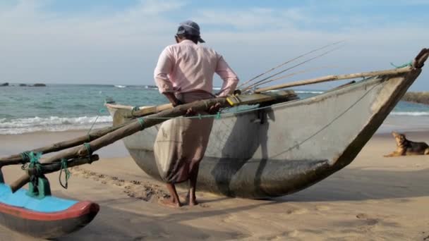 Homem puxa barco de pesca artesanal tradicional contra o mar — Vídeo de Stock