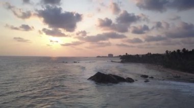 Beyaz köpüklü dalgalar kumlu sahilde ve kayalıklarda süzülüyor.