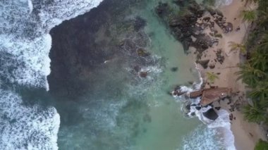 Köpüren okyanus dalgaları taşlarla dolu kumlu sahil şeridinde yuvarlanıyor.