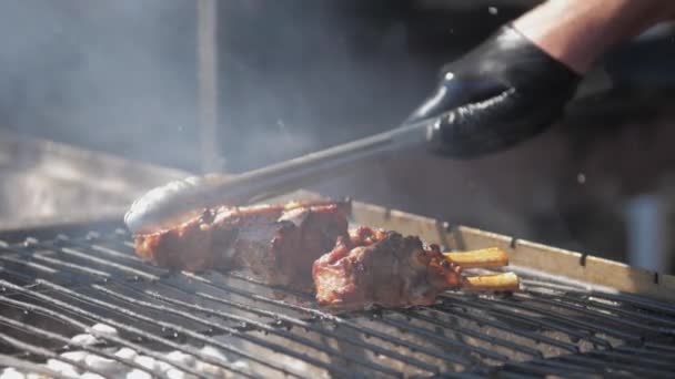 Person holds silver tongs and presses brown pork ribs — Stock Video