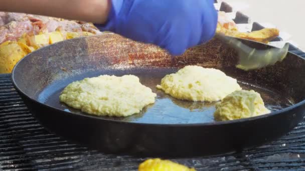 Человек в синих перчатках кладет картофельные оладьи на сковородку — стоковое видео