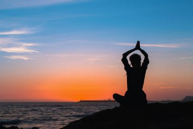 Yoga meditasyon sırasında şaşırtıcı günbatımı okyanus plaj Lotus pozisyonda kadın silüeti.