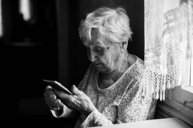 Yaşlı kadın ile smartphone elinde oturur. 