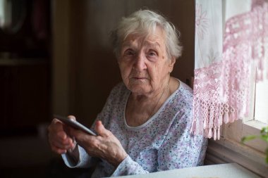 Yaşlı kadın evinde bir akıllı telefon ile.
