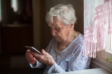 Yaşlı kadın evinde bir akıllı telefon ile.