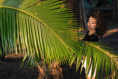 Genç karışık ırk kadın ve palmiye ağaçlarının yaprakları arasında.