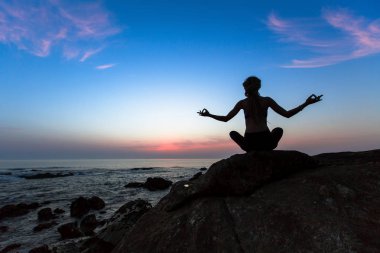 Yoga egzersizleri okyanus üzerinde günbatımında pratik bir genç kadın silüeti.