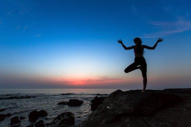 Yoga egzersizleri okyanus üzerinde günbatımında pratik bir genç kadın silüeti.